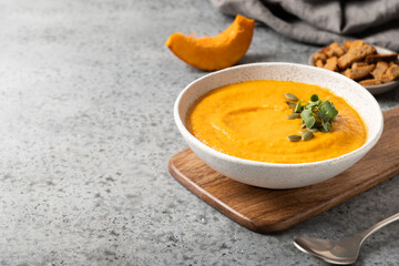 Fall pumpkin soup with cream garnish microgreens on grey background. Close up. Space for text.