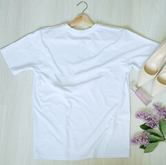 white t-shirt on a hanger and accessories, a bottle of perfume, a sprig of lilac and shoes, top view. Fashion, style, summer look, wardrobe