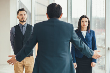 Angry boss standing back to the camera, shouting at his workers, raising hand, while stressed...