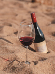 Red wine glass with bottle on the beach sand. Summertime, vacation, weekend