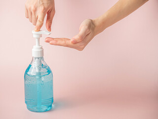 Woman finger press blue alcohol gel bottle on pink pastel background.