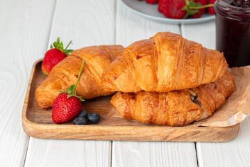Fresh croissant decorated with berries on white wooden board