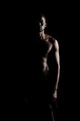 Fototapeta na wymiar Bare chested black fitness man silhouette looking at camera wearing sport short trousers on black backgorund