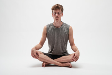 Fototapeta premium Young boy meditating with eyes closed and legs crossed on white background