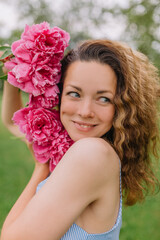 Naklejka premium girl model mother on her head curly curls holding peonies and flowers in her dress gently presses them to herself on the nature in the park