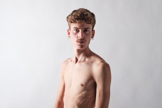 young blond boy bare chested with mustache and wearing earrings  standing looking at camera