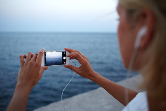 Cropped image of female tourist making photo of amazing sea view on cell telephone during summer trip, young woman taking picture of ocean landscape on her mobile phone while walking on the beach
