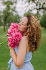 Fototapeta premium girl model mother holding peonies and flowers in her dress gently presses them to herself on the nature in the park