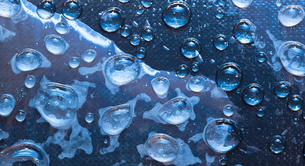 Light-blue ice particles and blue water droplets are located on a blue glass surface. Close-up. 