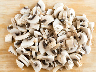 Sliced champignons on a wooden board. Edible mushrooms in pieces, top view