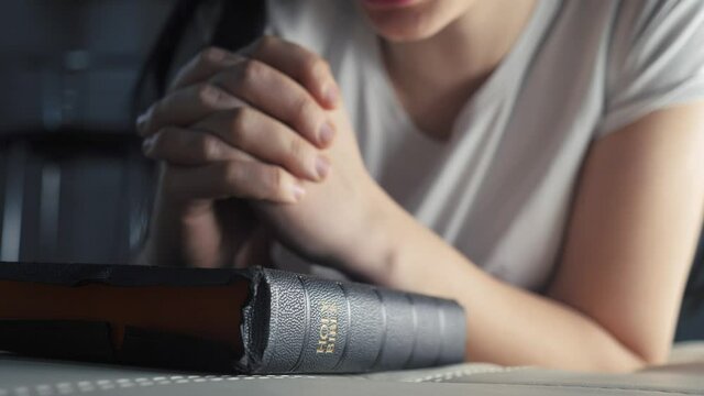 girl praying indoors at bedtime on bible. religion concept evening prayer woman brunette hands on lifestyle bible praying by bed