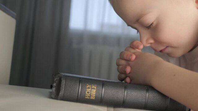 little boy praying bible. religion concept holy book bible. little boy prays at home in the evening by lifestyle the bed on the bible
