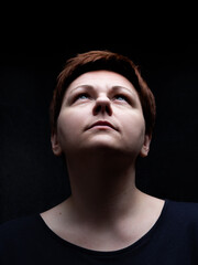 Portrait of short hair woman looking upward against black background. Spiritual expression on enlightened face, eyes focused on the light.