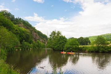 Obraz premium Beautiful landscape in Clécy (Normandy, France). People are kayaking/canoeing on the Orne River. We can see cliffs & verdant nature in the background. 