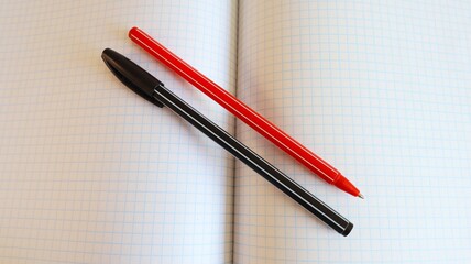 Red and black ballpoint pens on a sheet of squared notebook closeup with space for text