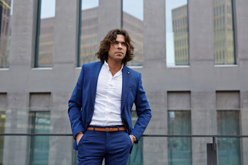 Portrait of handsome executive standing near office building with hands in his pockets