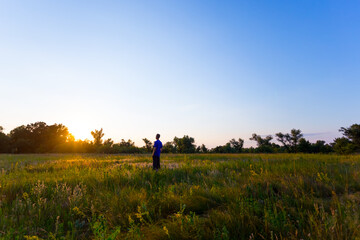Obraz na płótnie Canvas happy man see off evening sun among a green summer prairie, human emotion concept background