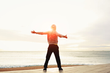 Freedom, relax and harmony in nature, Rear view of a young guy with his arms outstretched at the seaside standing next to the sea, happiness emotional concept