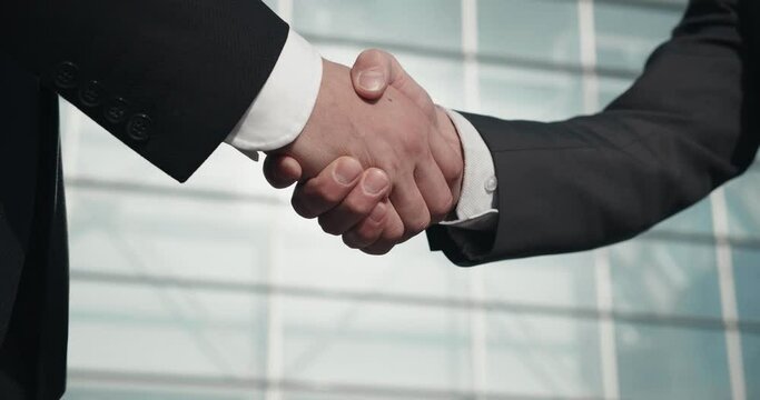Formal dressed two Businessmen speaking and walking outside Office Building. Office worker shows his Luxury Wristwatch to his Colleague. Men holding Mobile Phones and wearing classical clothes.