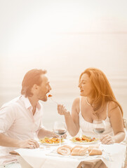 Happy couple rest in beach cafe. Mature woman feeding her man. Care for loved ones concept. Romantic concept. Tinted image.