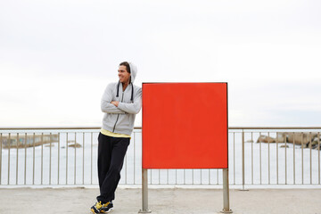 Young male jogger took break after run outdoors while standing near red board with copy space area...