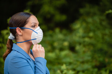 Beautiful girl puts a medical mask on her face on the nature. Coronavirus and Covid-19 Protection