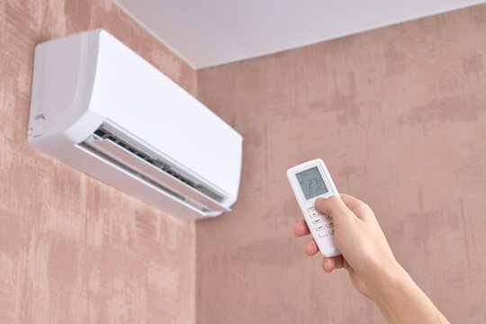 air conditioner at domestic room. heat temperature indoors. person holds remote control for aircon. heat or cold at home.