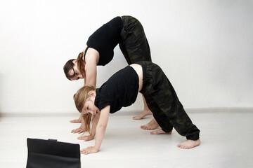 Mother and daughter are doing yoga online. Woman and little girl are in the mountain pose