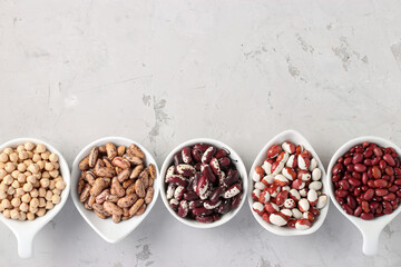 Four varieties of beans and chickpea - protein rich beans are located on a gray concrete background, Top view, Copy space
