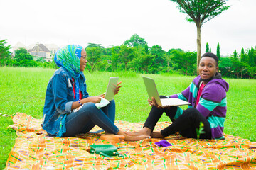 young black couples sitting down in a park, using their laptops to surf the internet