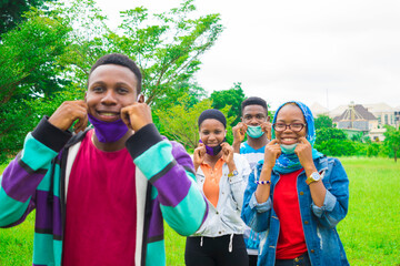 young black friends standing while trying to wear their nose masks in a park