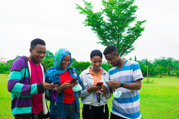 young black friends holding their nose masks and using their phones in a park