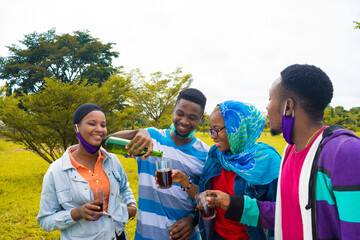 young black people standing in a park and pouring drinks into their glass cups