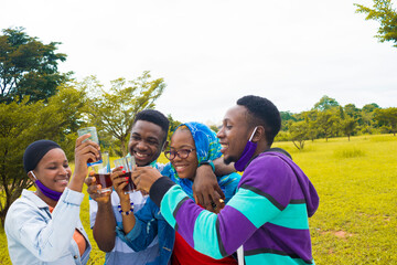 young black people standing in a park, giving a toast with drink in their glass cups