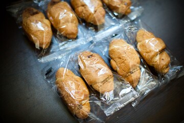 Factory made packaged croissants. Mass production products. The production dates and the last consumption dates are written on the packages. Blurry and black background. 