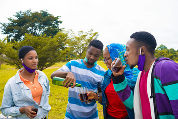 young black people standing in a park and pouring drinks into their glass cups