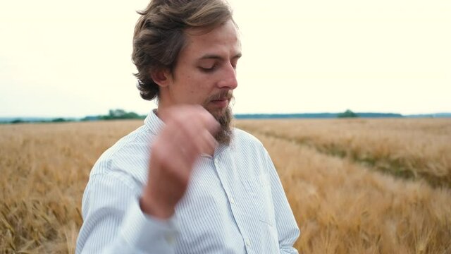 30-year-old stylish male agronomist with a beard stands in the field and writes data to a tablet. Harvest inspection