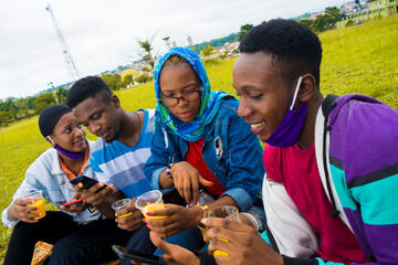 young black people sitting in a park, drinking from their glass cups and using smartphone