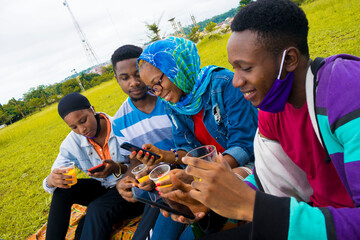 young black people sitting in a park, drinking from their glass cups and using smartphone