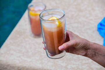 A person holding a class with a colorful  drink and lemon.