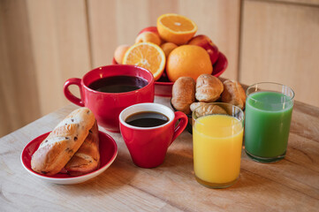 Breakfast with black coffee, croissant, fruit, orange juice and green juice on a wooden table