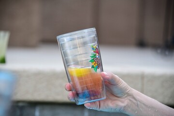 A person holding a class with a colorful  drink and lemon.