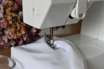 A fragment of a white electric sewing machine on a table in the scenery. Sews white cloth. Advertising sewing equipment. The controls of the sewing machine. Home crafts. Tailoring. Beautiful backgroun