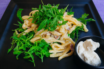 spaghetti pasta with pesto sauce and arugula leaves on a square