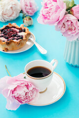 Summer romantic breakfast.White cup of coffee,cake with berries,open book and peonies on a blue background.Good morning concept.Selective focus with shallow depth of field