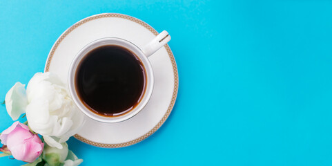 White cup of coffee and white and pink peony flowers on a blue background.Summer romantic breakfast.Good morning concept.Selective focus, copy space, top view