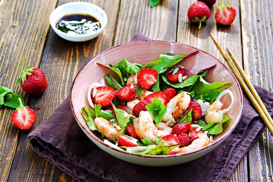 Salad with fresh strawberries, fried shrimp and young beet tops in a pink bowl on a wooden background.