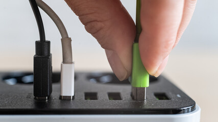 Modern convenient multi-port usb charger for devices. Close-up of a female hand plugging multi-colored cables into a power outlet. Macro.