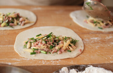 three rolled-up dough circles stuffed with cheese, ham and greens on a wooden board sprinkled with flour