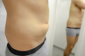 naked man body in underwear standing in front of mirror with big belly and visible love handles recognizing not being slim
